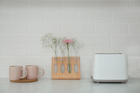 Modern toaster, cups and flowers on counter in kitchenの写真素材