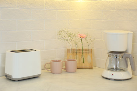 Modern toaster, cups, flowers and coffee machine on counter in kitchenの写真素材