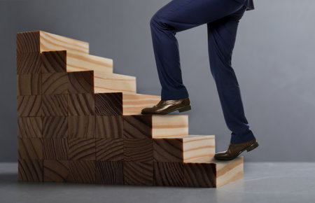 Businessman walking up stairs against grey background, closeup. Career ladder concept