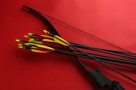 Black bow and set of arrows on red background, flat lay. Archery sports equipmentの写真素材