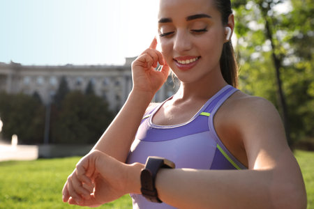Woman checking fitness tracker after training in park, closeup