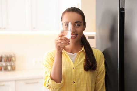 Young woman looking through glass of pure water in kitchenの写真素材