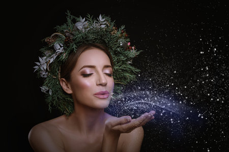 Beautiful young woman with Christmas wreath blowing kiss on black backgroundの写真素材