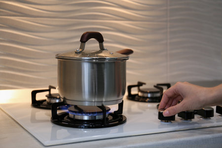 Woman cooking food in pot on modern kitchen stove with burning gas indoors, closeupの写真素材