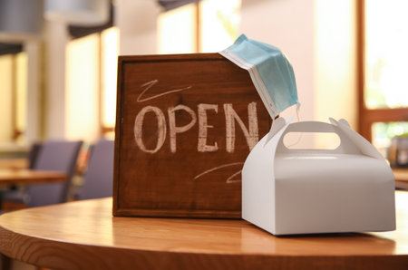 OPEN sign, packed takeout order and protective mask on table in restaurant.