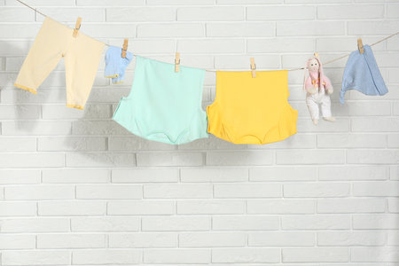 Baby clothes hanging on washing line near white brick wallの写真素材
