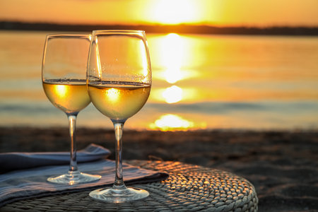 Glasses of delicious wine on riverside at sunsetの写真素材