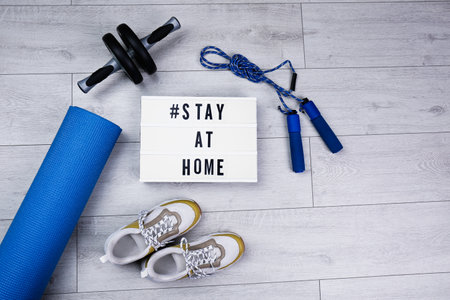 Sport equipment and lightbox with hashtag STAY AT HOME on floor, flat lay. Message to promote self-isolation during COVIDâ19 pandemicの写真素材