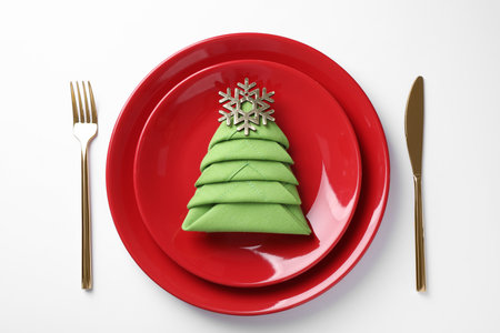 Festive table setting with green napkin folded in shape of Christmas tree on white background, top viewの写真素材