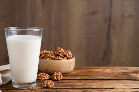 Glass of walnut milk on wooden table, space for textの写真素材
