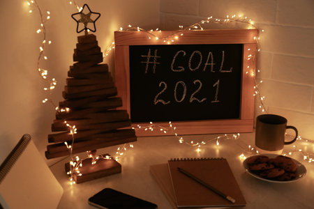 Chalkboard with hashtag Goal 2021, fairy lights near notebooks, smartphone and cookies on white table. New year targetsの写真素材