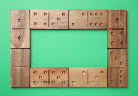 Frame made of wooden domino tiles on green background, flat lay. Space for textの写真素材