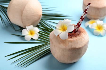 Fresh coconut with drinking straws and flowers on light blue backgroundの写真素材