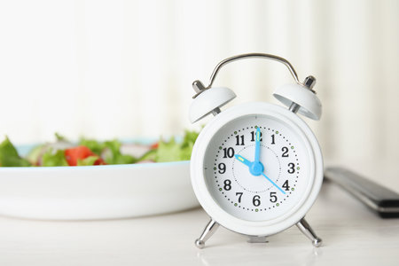 Alarm clock and plate with salad on white table. Meal timing concept
