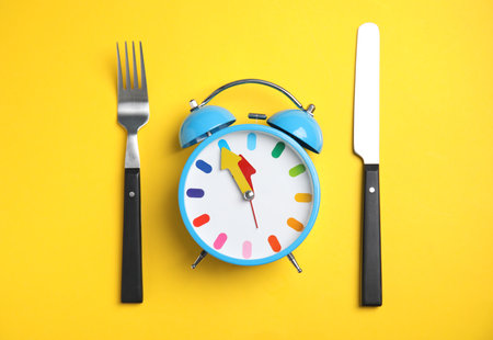 Alarm clock and cutlery on yellow background, flat lay. Diet regimeの写真素材