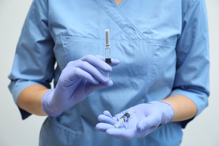 Doctor holding syringes with COVID-19 vaccine on light background, closeupの写真素材