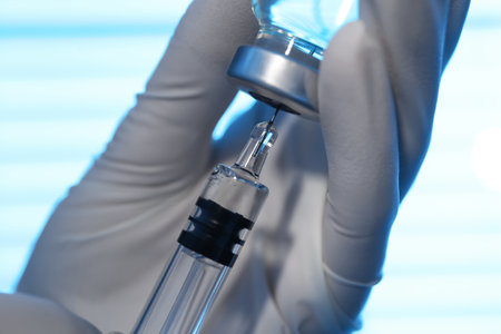 Woman filling syringe with vaccine from vial on blurred background, closeupの写真素材