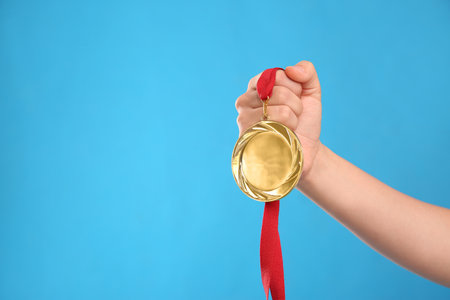 Woman holding gold medal on light blue background, closeup. Space for textの写真素材