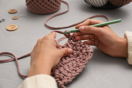Woman crocheting with threads at gray table, closeup. Engaging hobbyの写真素材