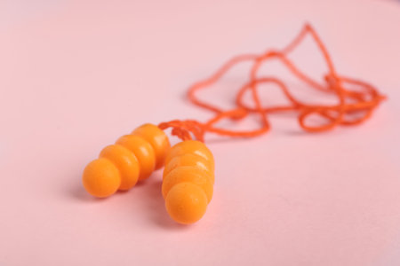 Pair of orange ear plugs with cord on pink background, closeupの写真素材