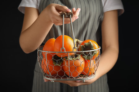 Woman holding delicious fresh persimmons on black background, closeupの写真素材