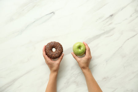 Top view of woman choosing between donut and healthy apple on white marble table, closeupの写真素材