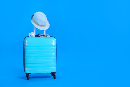 Travel suitcase with hat, camera and glasses on light blue background, space for text. summer holidaysの写真素材