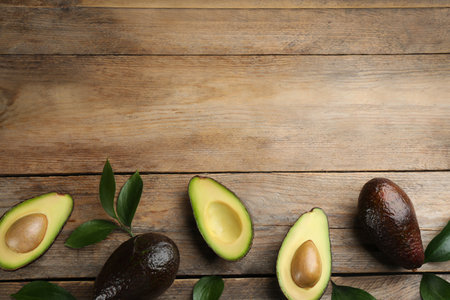 Whole and cut avocados with green leaves on wooden table, flat lay. Space for textの写真素材