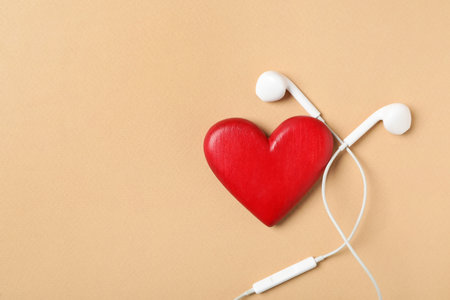 Modern earphones and red heart on beige background, flat lay with space for text. Listening love music songsの写真素材