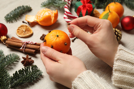Woman decorating tangerine with cloves at light wooden table, closeup. Christmas atmosphereの写真素材