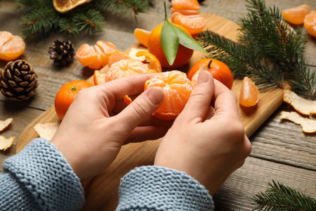 Woman peeling fresh tangerine at wooden table, closeup. Christmas atmosphereの写真素材