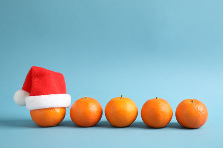 Row of fresh tangerines and one with Christmas hat against light blue background. Space for textの写真素材