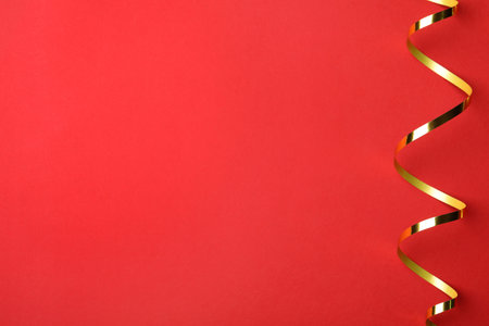 Shiny golden serpentine streamer on red background, top view. Space for textの写真素材