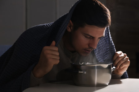 Man with plaid doing inhalation above saucepot at table indoorsの写真素材