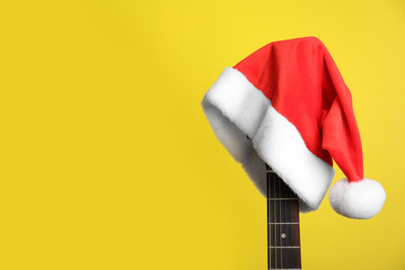 Guitar with Santa hat on yellow background, space for text. christmas music conceptの写真素材