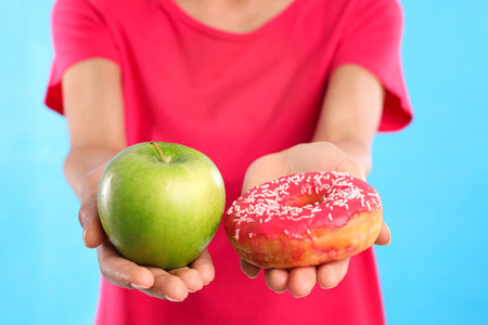 Woman choosing between donut and fresh apple on light blue background, closeupの写真素材
