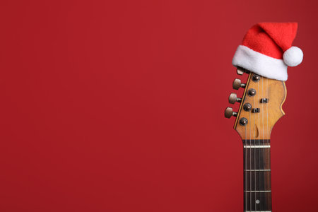 Guitar with Santa hat on red background, space for text. Christmas music conceptの写真素材
