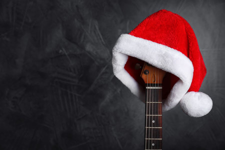 Guitar with Santa hat on black background, space for text. Christmas musicの写真素材