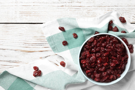 Tasty dried cranberries in bowl on white wooden table, flat lay. Space for textの写真素材