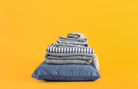Stack of clean bed sheets and pillow on yellow backgroundの写真素材