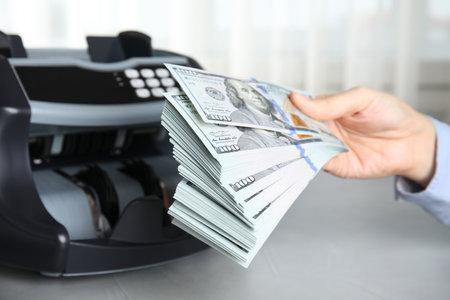 Woman holding money near counting machine at table indoors, closeupの写真素材