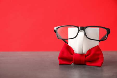 Funny composition with bow tie, glasses and cup on grey table against red background. Space for textの写真素材