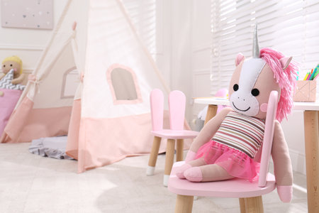 Cute toy unicorn on chair in stylish playroom, space for textの写真素材