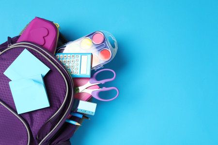 Purple backpack with different stationery on light blue background, top view and space for text. back to schoolの写真素材