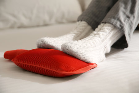 Person warming feet with hot water bottle on bed, closeupの写真素材