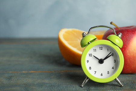 Alarm clock, orange and apple on light blue wooden table, space for text. Meal timing conceptの写真素材