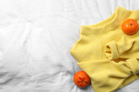 Beautiful yellow warm sweater and tangerines on white bedsheet, flat lay. Space for textの写真素材