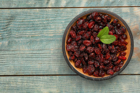 Tasty dried cranberries and leaves in bowl on blue wooden table, top view. Space for textの写真素材