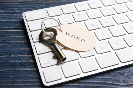 Key with tag WORD and computer keyboard on blue wooden table, closeup. Keyword conceptの写真素材