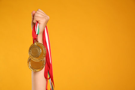 Woman holding gold medals on yellow background, closeup. Space for textの写真素材